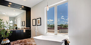 Luxurious bathroom with large vanity mirrors, a standalone tub, and two large windows overlooking desert.